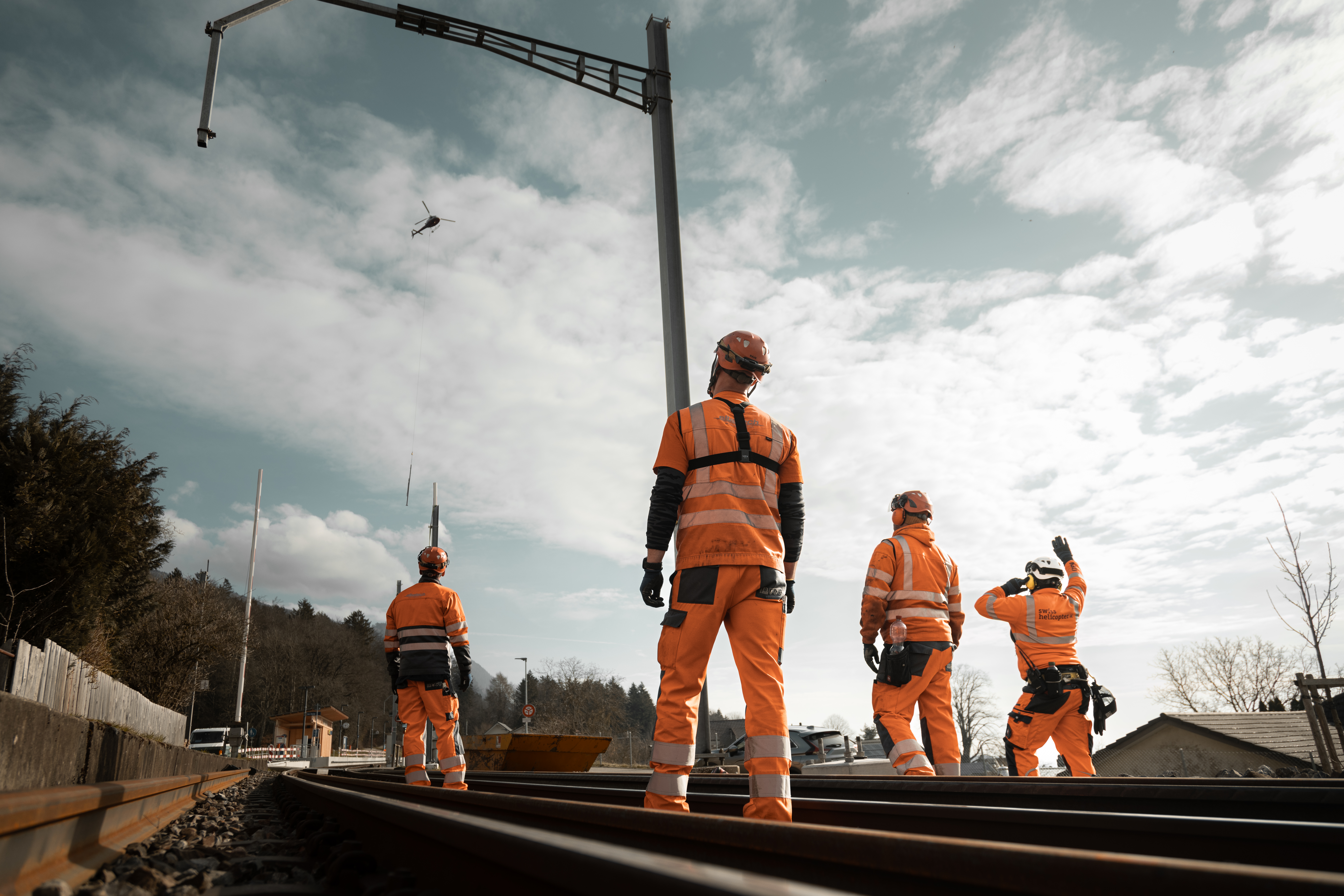 Mehrere Mitarbeitende warten bei der Baustelle auf den Helikopter mit Masten.